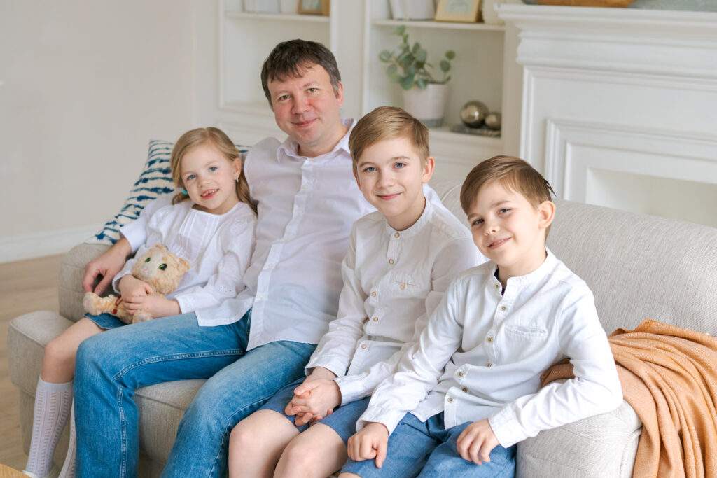 Cheerful father with laughing children looking at camera sitting on couch